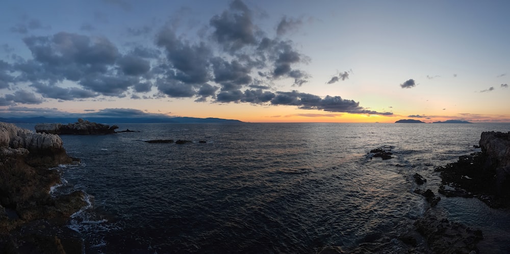 a body of water with rocks and a sunset in the background