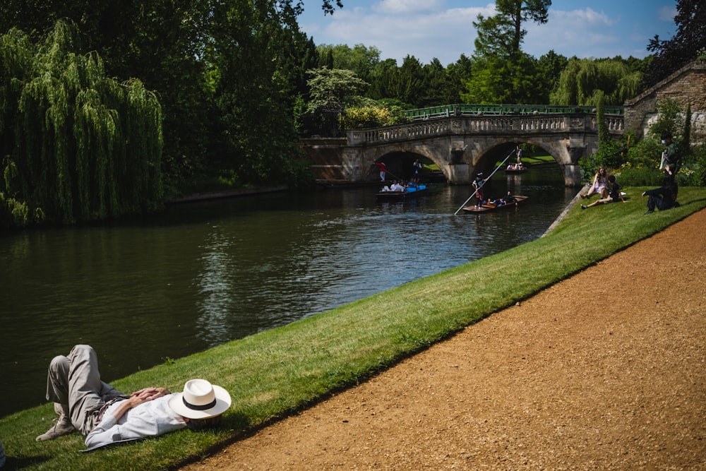 a person lying on the grass next to a river with a bridge