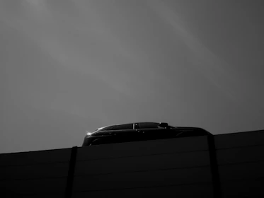 Modern car silhouette framed by minimalist architectural lines under a clear blue sky.