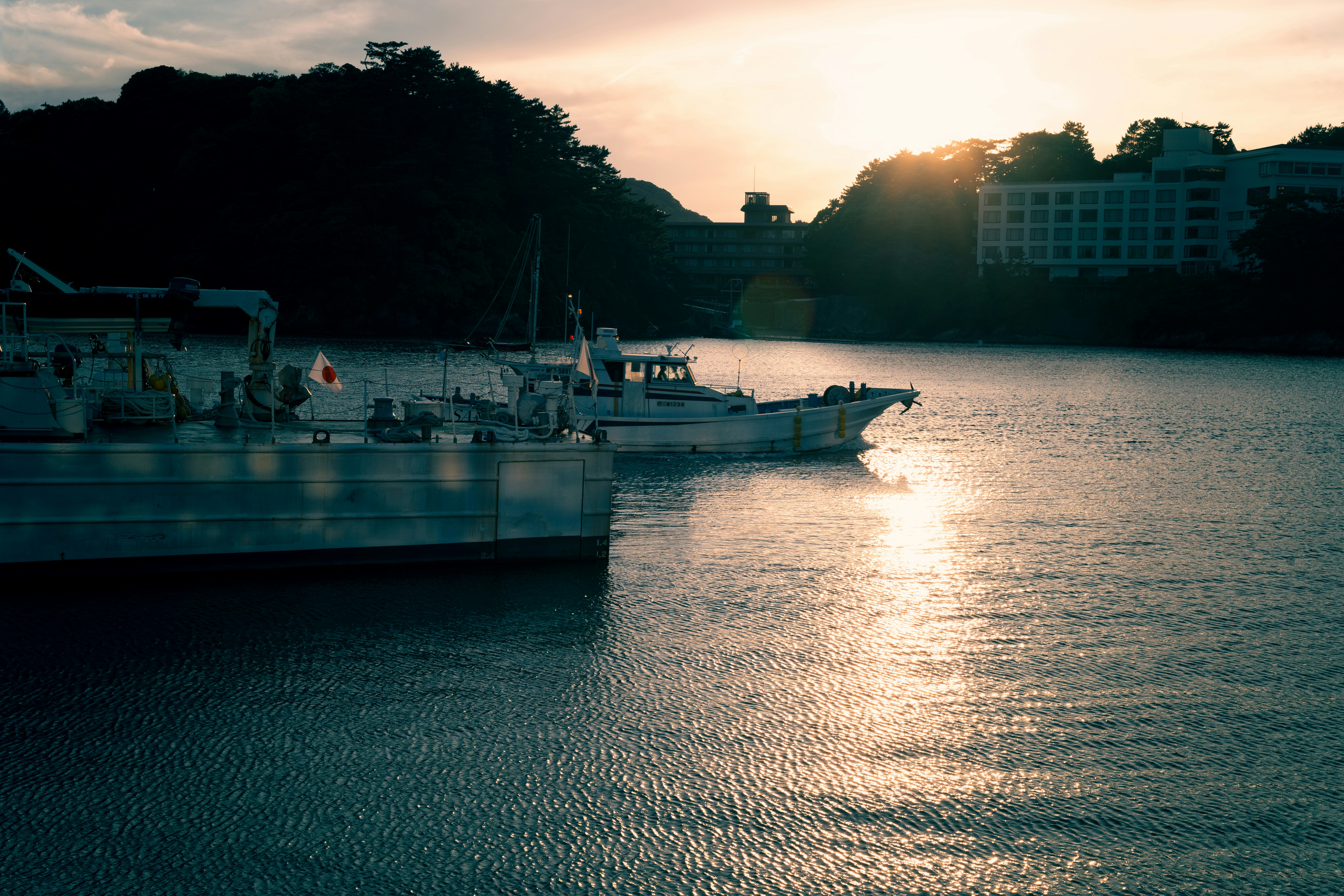 Two boats travel across water near hills at sunset.