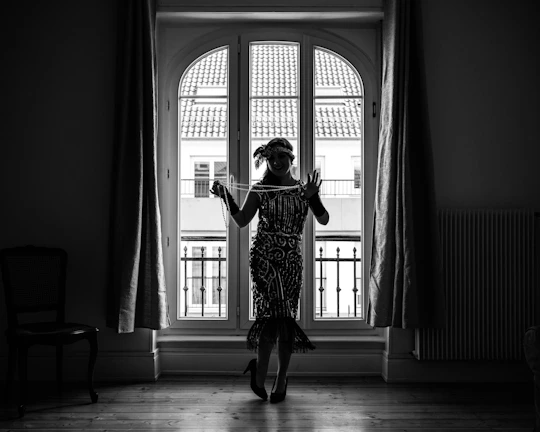 Editorial style photo of a woman wearing a statement feminine piece in muted rose tones, standing by a large window.