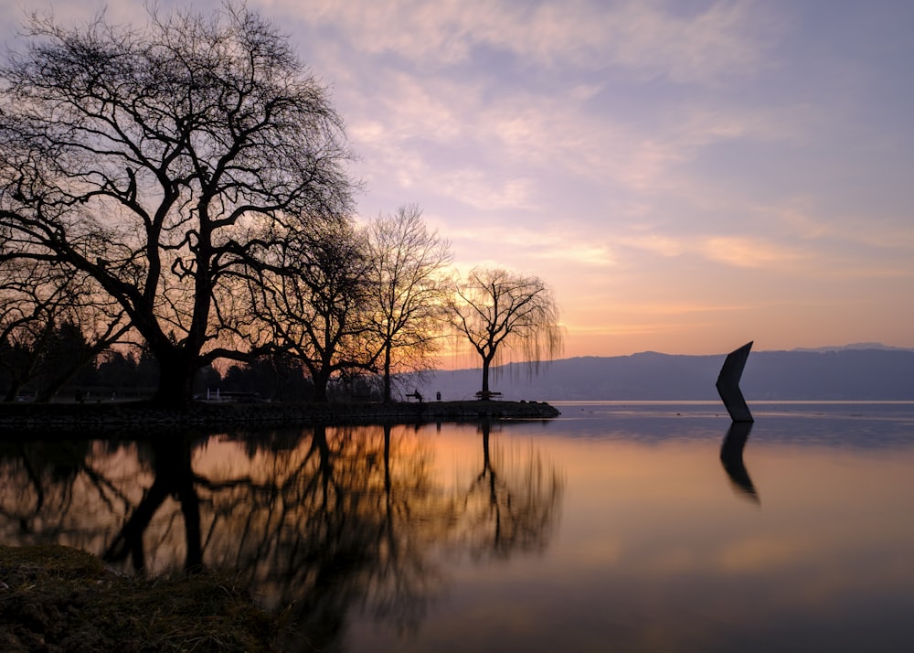 a body of water with trees and a sunset in the background