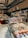 A well-stocked supermarket aisle features shelves filled with various packaged foods, including chocolates and snacks. Refrigerated displays contain assorted prepared meals and desserts. Overhead lights and exposed ductwork give the space an industrial feel.