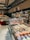 A well-stocked supermarket aisle features shelves filled with various packaged foods, including chocolates and snacks. Refrigerated displays contain assorted prepared meals and desserts. Overhead lights and exposed ductwork give the space an industrial feel.