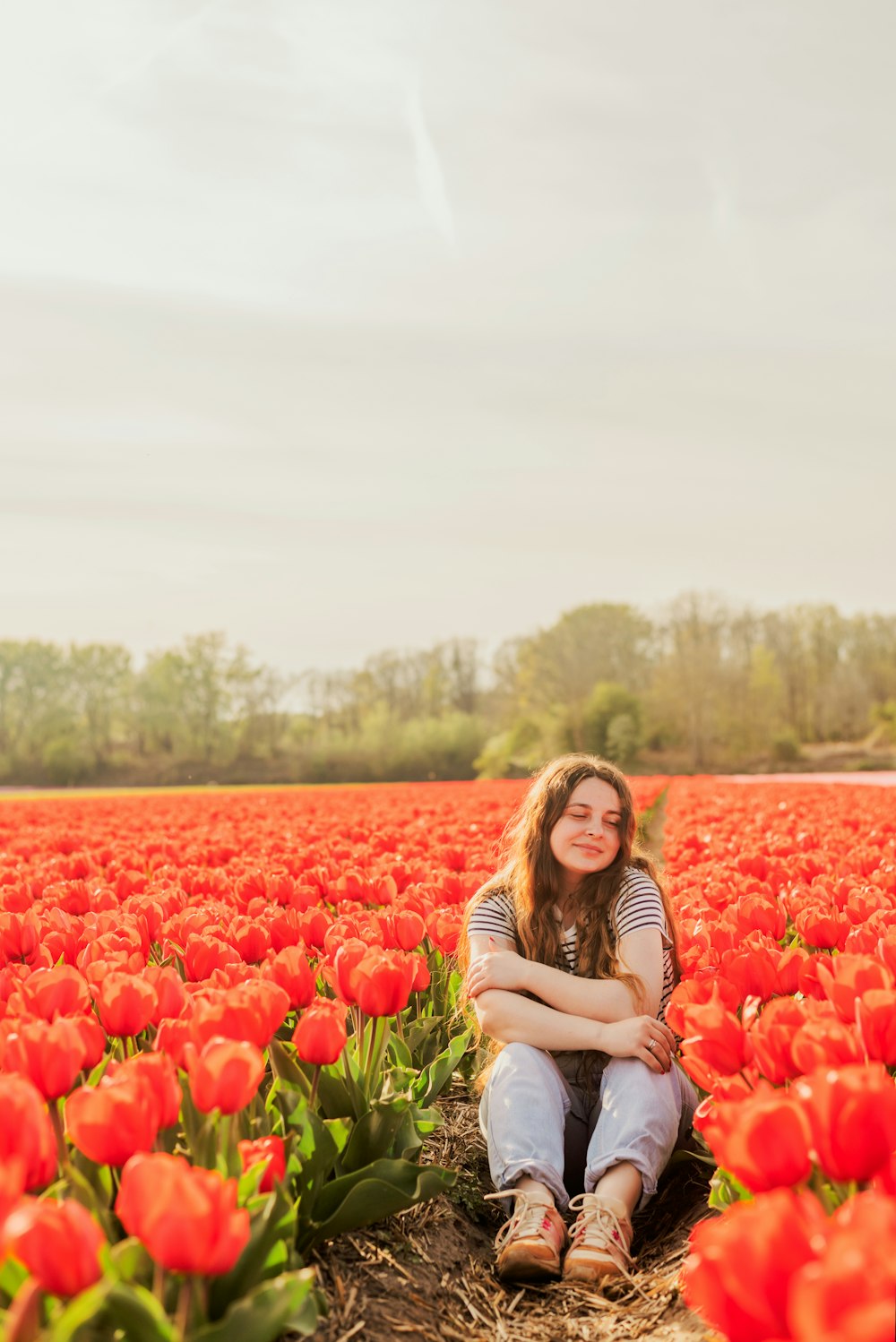 a woman sitting in a field of red flowers