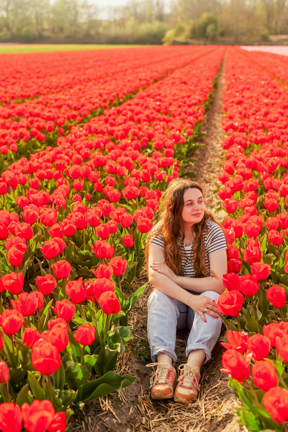 a woman sitting in a field of red flowers