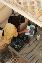 A happy person wearing headphones, mixing music on a laptop with vibrant orange and purple decor.