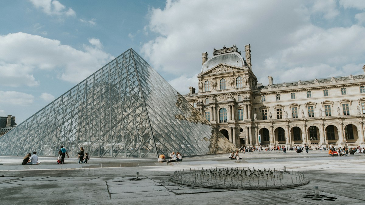 La pyramide de verre et le palais du Louvre à Paris, avec des visiteurs dans la cour Napoléon un jour de beau temps