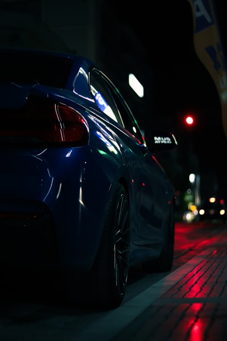 A sleek black luxury car with subtle blue metallic highlights parked in front of a modern cityscape at dusk.