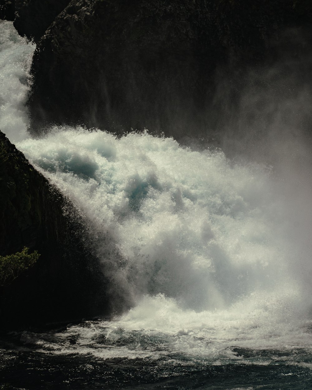 a large waterfall with a large rock in the foreground