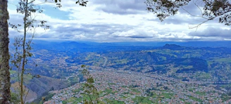 Panoramic view of Monterrey cityscape framed by lush green mountains under a clear blue sky.