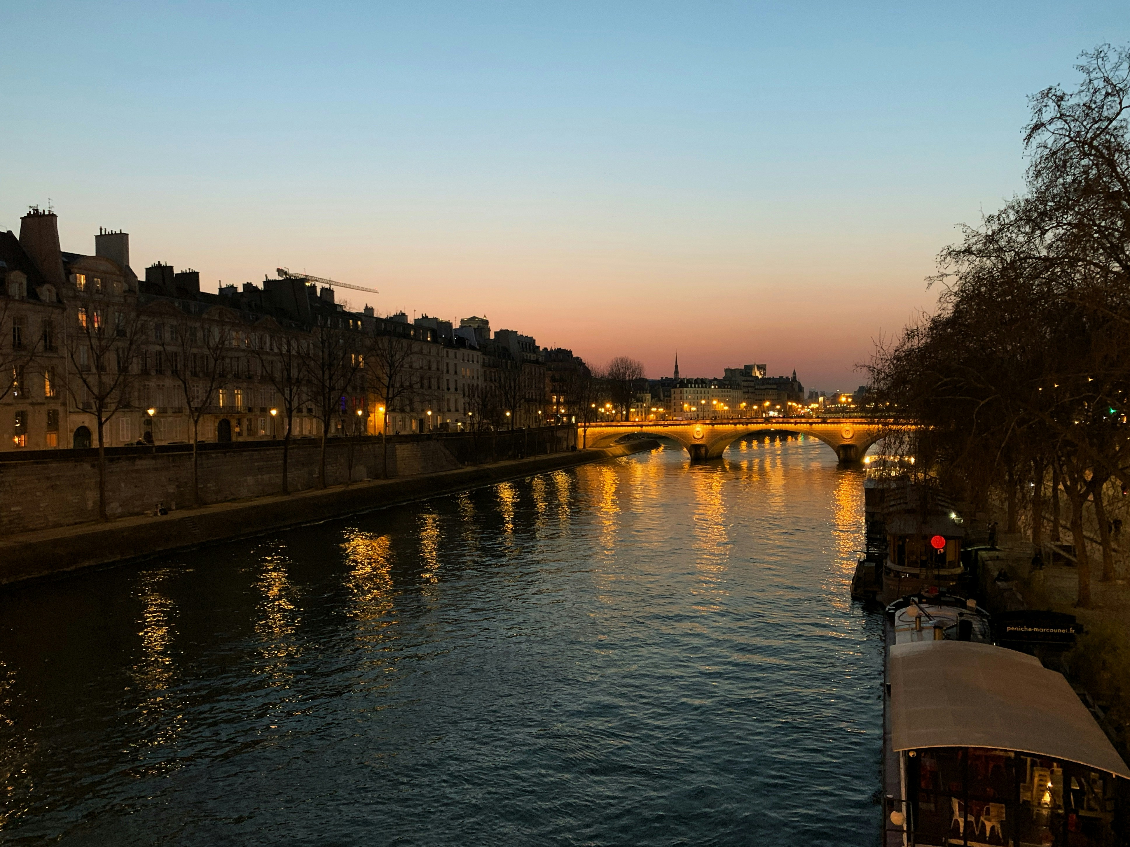 a river with a bridge and buildings along it, Sunset over La Seine, Paris.