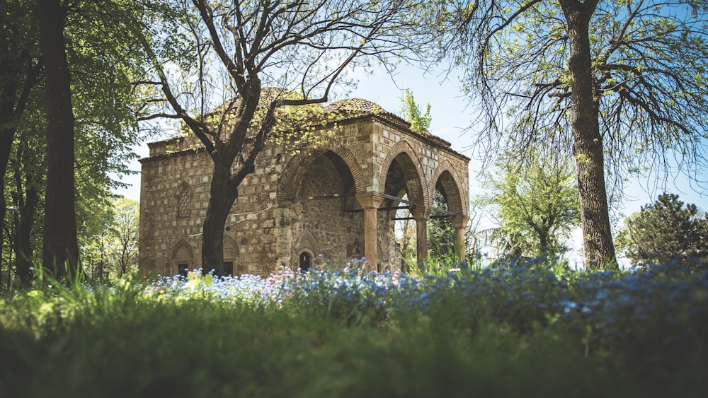 a stone building with arched windows surrounded by trees and flowers