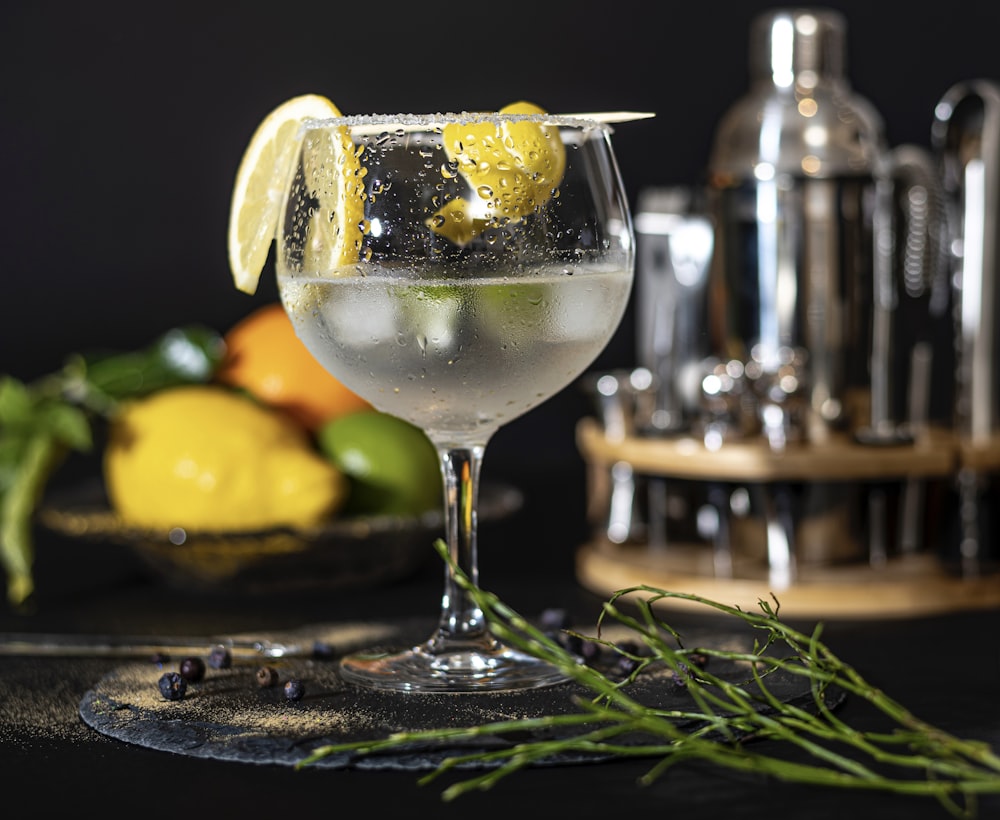 a glass of white wine with lemons and a lemon slice on a table