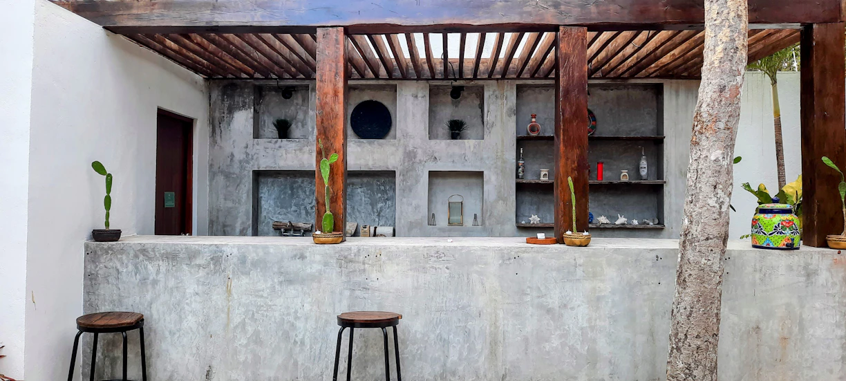 A cozy patio setup featuring a wooden outdoor bar table with counter height stools and a multi-tier plant stand adorned with vibrant greenery.