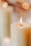 Close-up of a lit soy candle with soft glowing flame on a wooden surface.