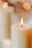 Close-up of a lit soy candle with soft glowing flame on a wooden surface.