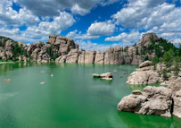 a body of water with rocks and trees around it with Sylvan Lake in the background