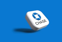 A three-dimensional white square block with rounded edges, featuring a blue geometric logo and the word 'CHASE' in black text. The block casts a shadow on a solid blue background.