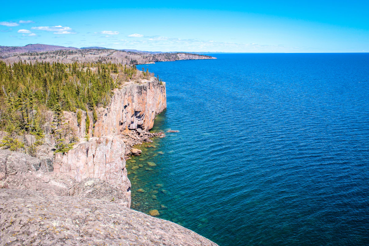 Pink rock cliffs at Palisade Head dropping into clear blue Lake Superior, with the shoreline receding into the distance