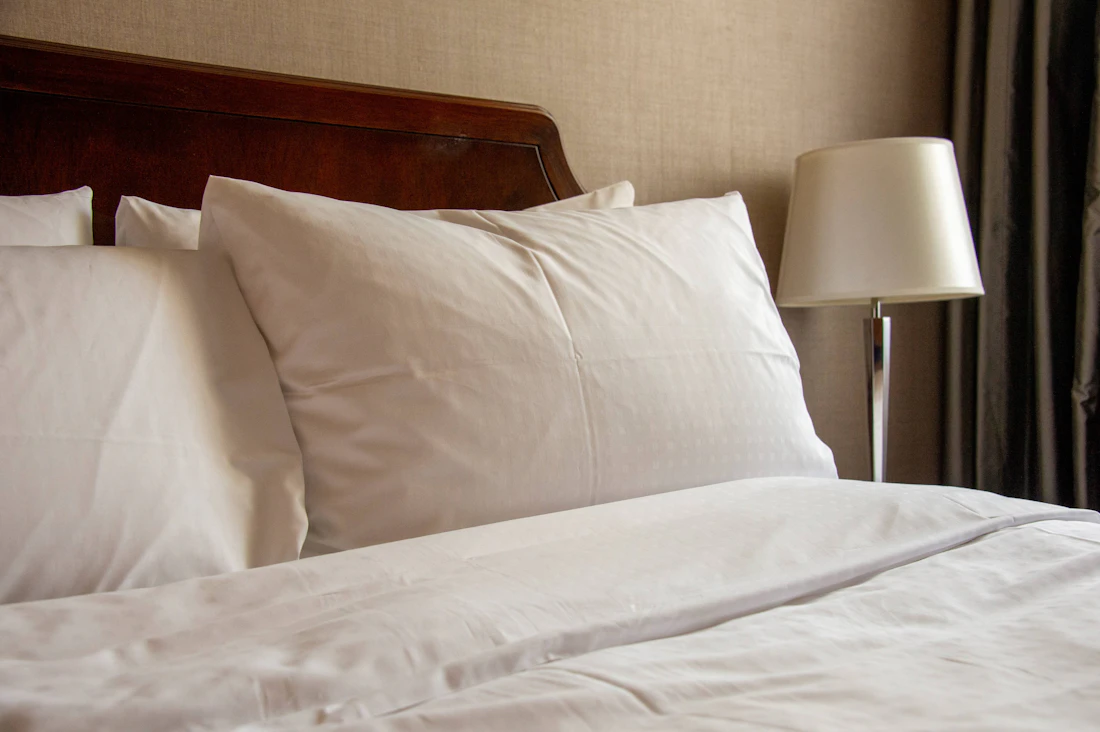 White pillows on a bed beside a warm bedside lamp