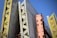 A structural framework composed of large, vertical concrete panels supported by wooden and metal beams. The beams are prominently yellow and orange, creating contrasting lines and textures against a clear blue sky.