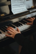 Close-up of hands playing piano keys with sheet music in background