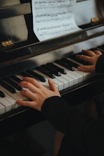 Close-up of hands playing piano keys with sheet music in the background.