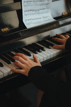 Close-up of hands playing piano keys with sheet music in the background.