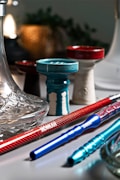 A collection of colorful hookah components arranged on a surface, including a decorative glass base, ceramic bowls in various colors, and metal stems with a shiny finish.