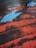 A cracked asphalt surface is painted with striking red lines and features a prominent blue arrow pointing to the right. The weathered texture of the paint contrasts sharply with the dark tarmac, creating a vivid and dynamic visual effect.
