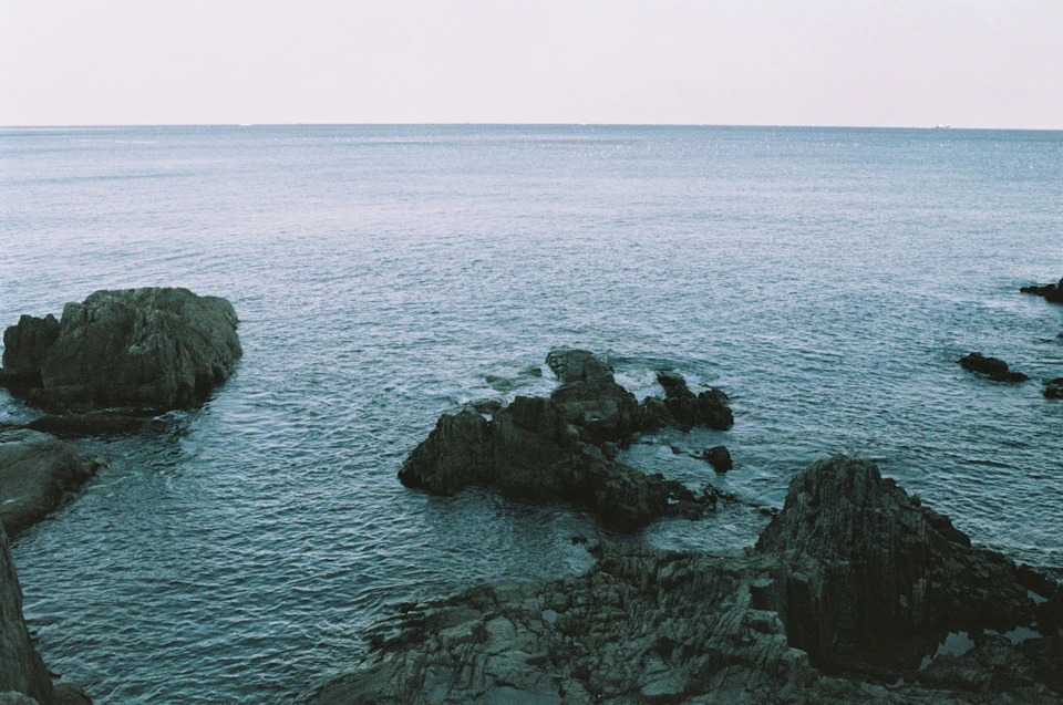Serene coastal scene with rocky shoreline and calm blue water under overcast sky conditions