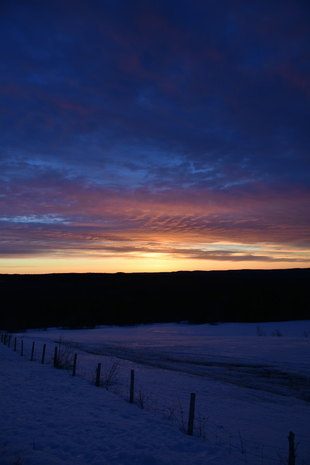 a snowy field with a fence and a sunset in the background