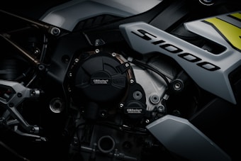 A close-up view of a high-performance motorcycle engine with the label 'S1000' prominently displayed. The image features detailed components like bolts, metallic surfaces, and branding of GB Racing and BMW. The design appears sleek and modern, emphasizing the intricate mechanical engineering.