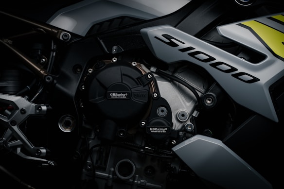 A close-up view of a high-performance motorcycle engine with the label 'S1000' prominently displayed. The image features detailed components like bolts, metallic surfaces, and branding of GB Racing and BMW. The design appears sleek and modern, emphasizing the intricate mechanical engineering.