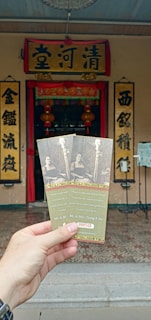 The image depicts a hand holding three tickets in front of an ornate entrance with Chinese characters on signs and lanterns. The tickets feature a black and white photo of a man and a woman, along with some text and the visible serial number 000745.