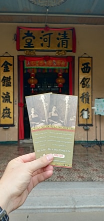 The image depicts a hand holding three tickets in front of an ornate entrance with Chinese characters on signs and lanterns. The tickets feature a black and white photo of a man and a woman, along with some text and the visible serial number 000745.
