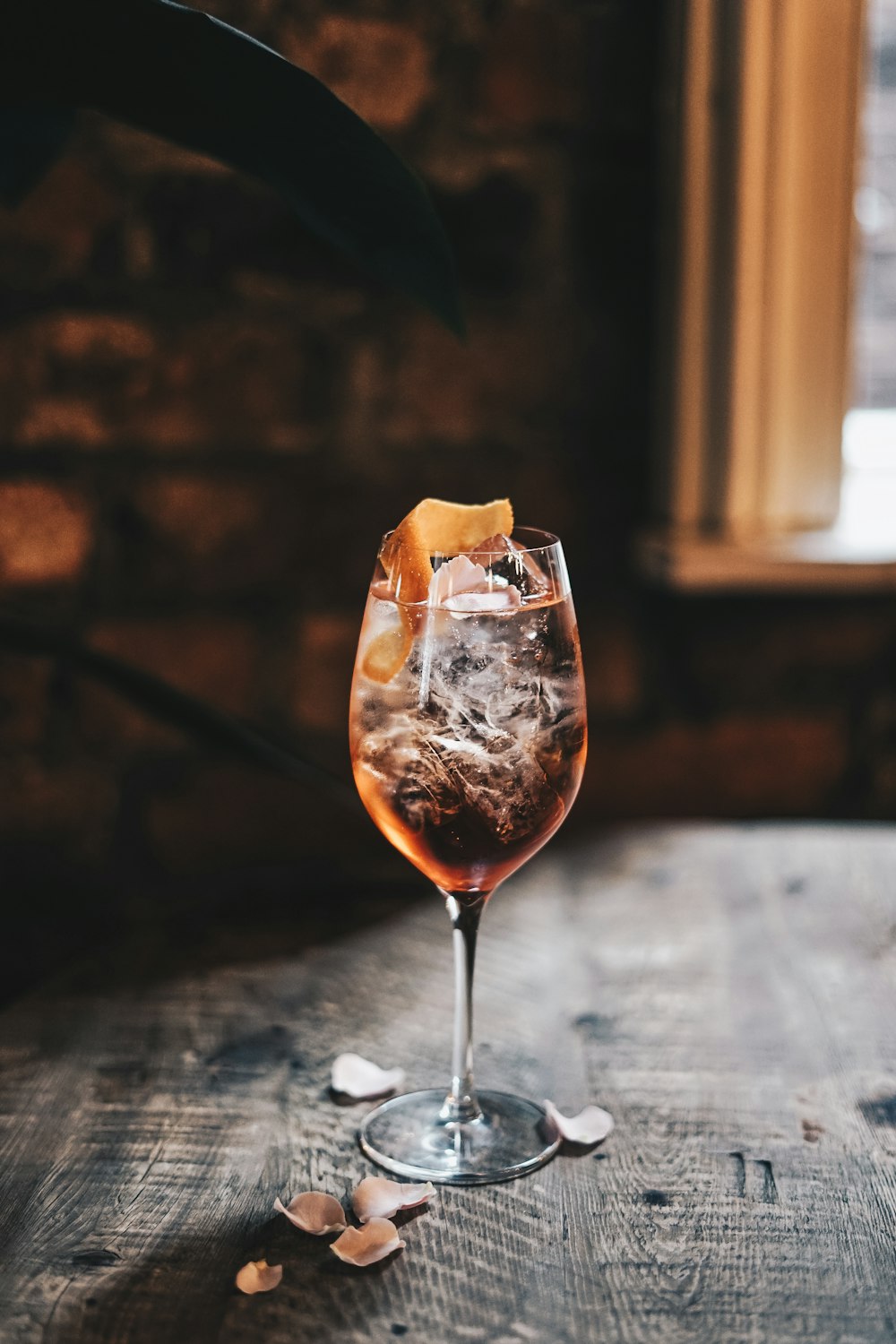 a glass of wine with ice and a slice of orange on a table