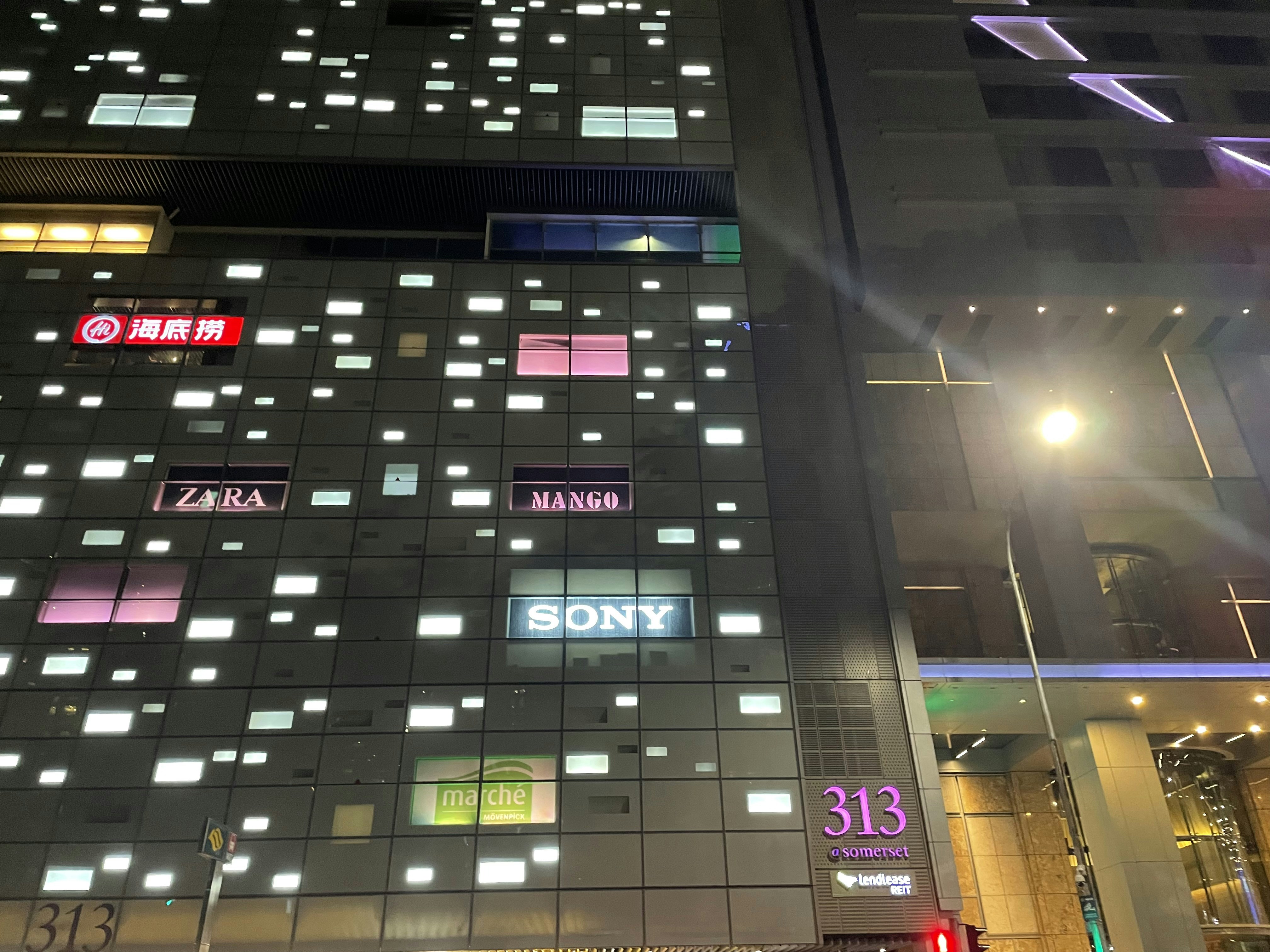 Modern illuminated shop front signage with 3D letters glowing blue on dark brick wall at night, commercial district