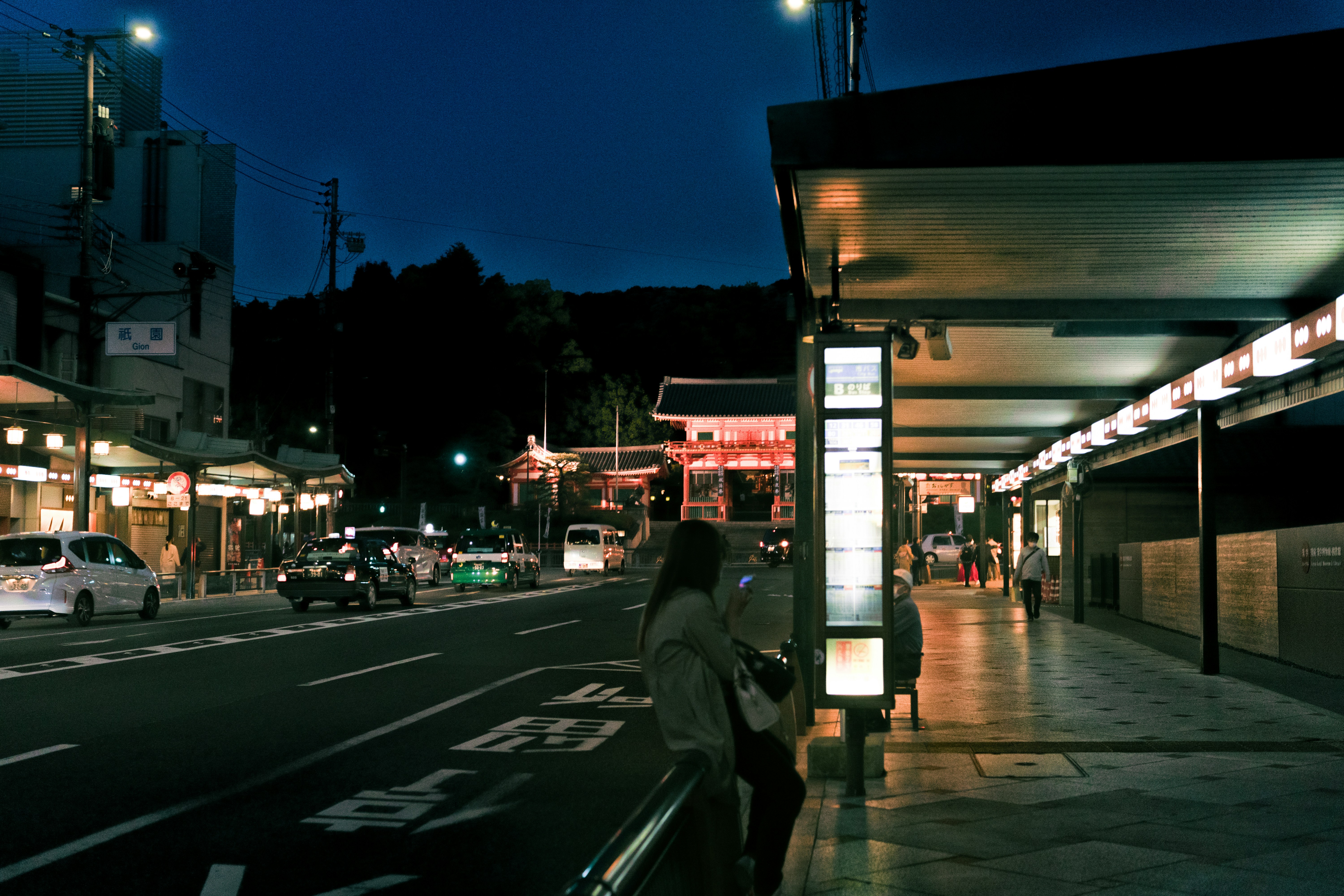 a person standing on a sidewalk next to a street with cars and buildings, 