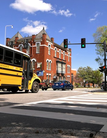 A crossing guard in a high visibility vest guiding children across a crosswalk near a school bus