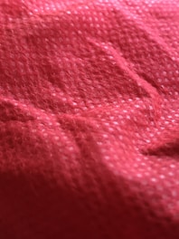 Close-up view of a red textured fabric surface with a grid-like pattern and visible fibers.
