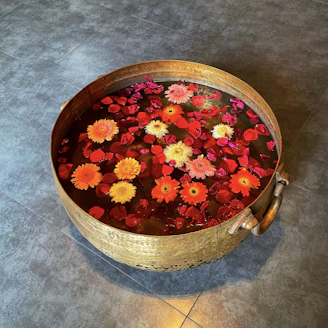 A beautifully crafted brass urli filled with vibrant floating flowers, placed at a warmly lit entrance.