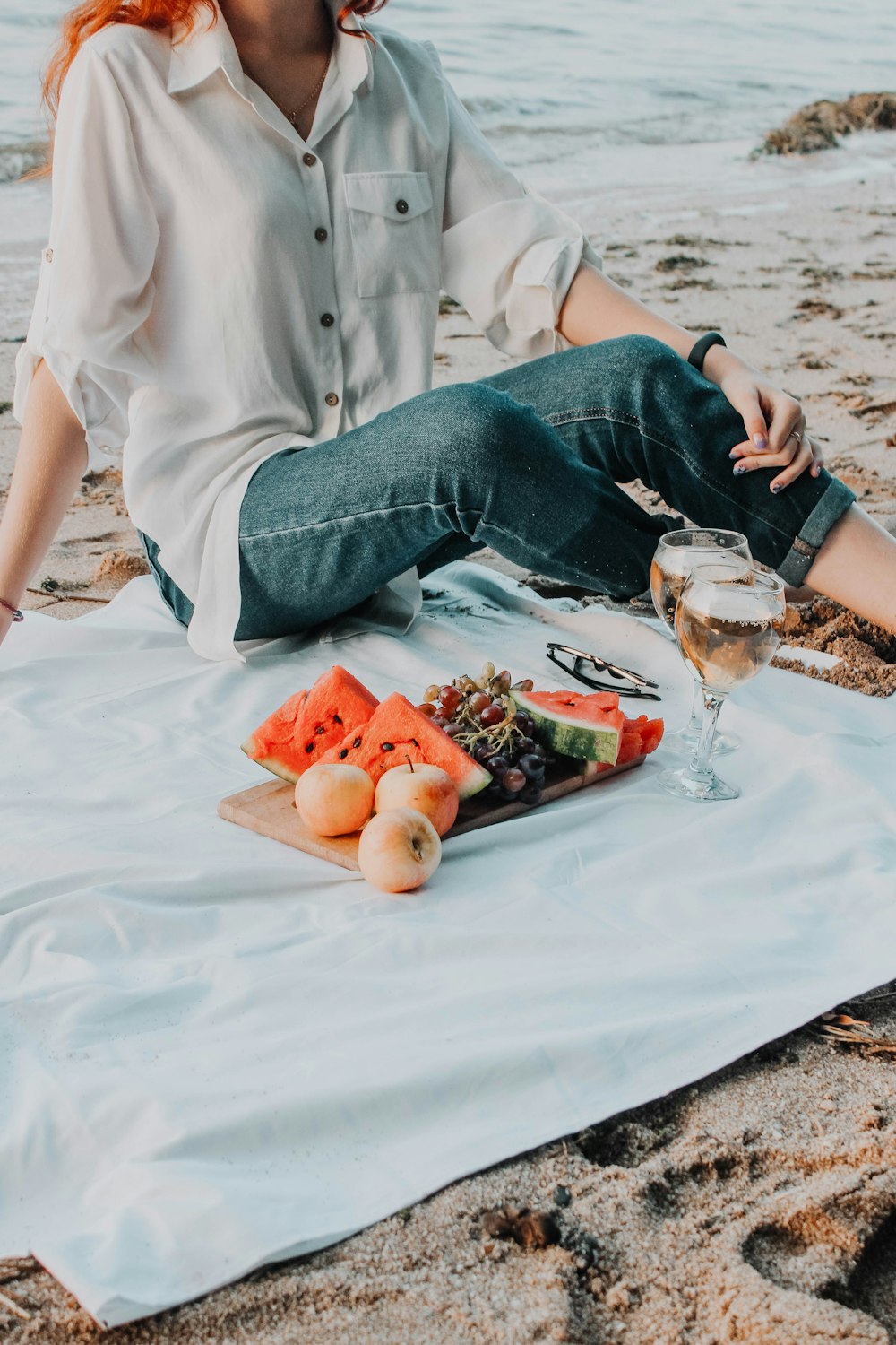 a person sitting on a beach with food and a glass of beer