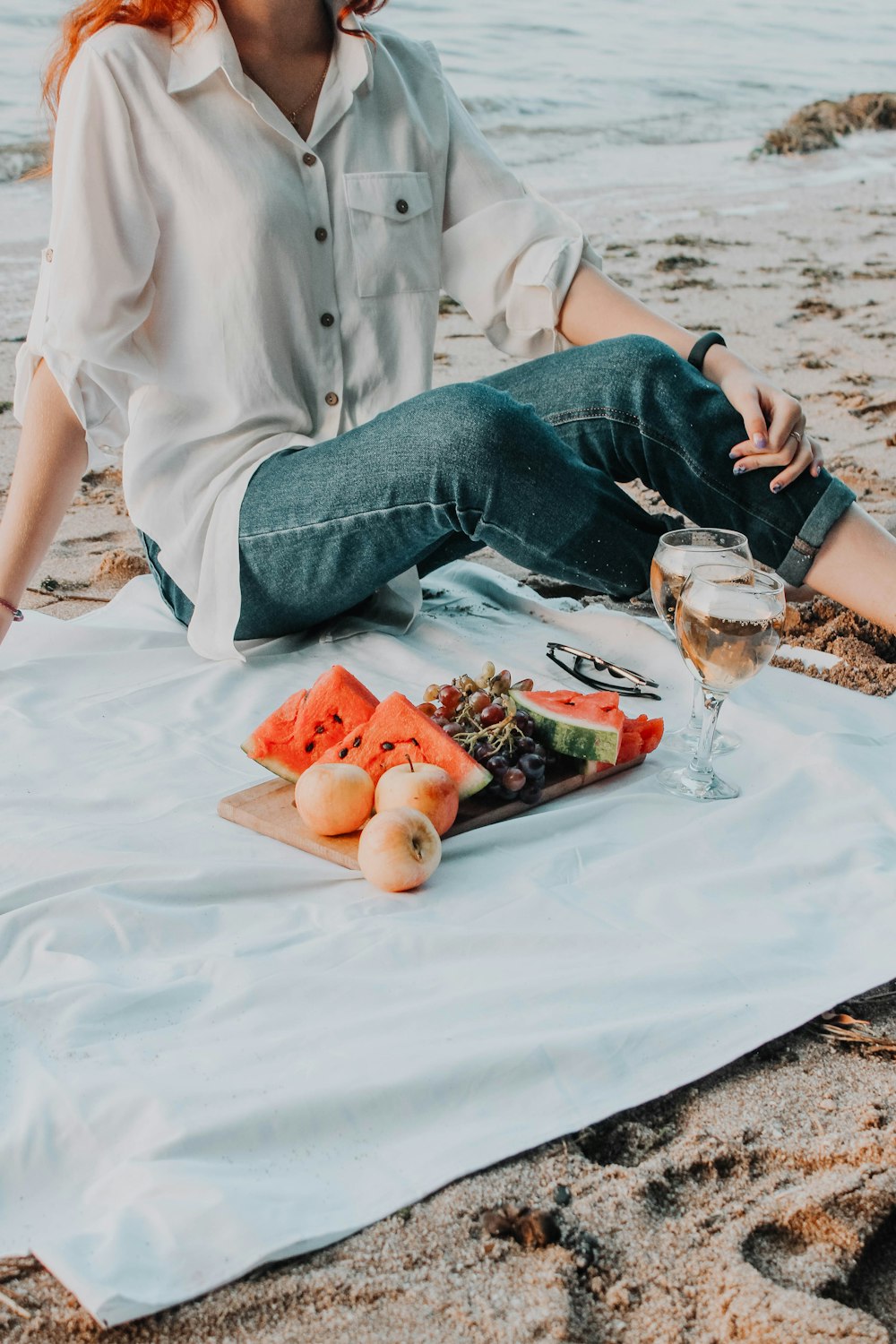 una persona seduta su una spiaggia con cibo e un bicchiere di birra