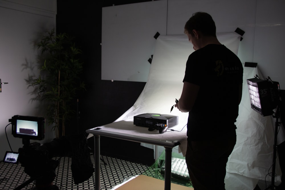 a man standing in front of a desk with a computer and a plant