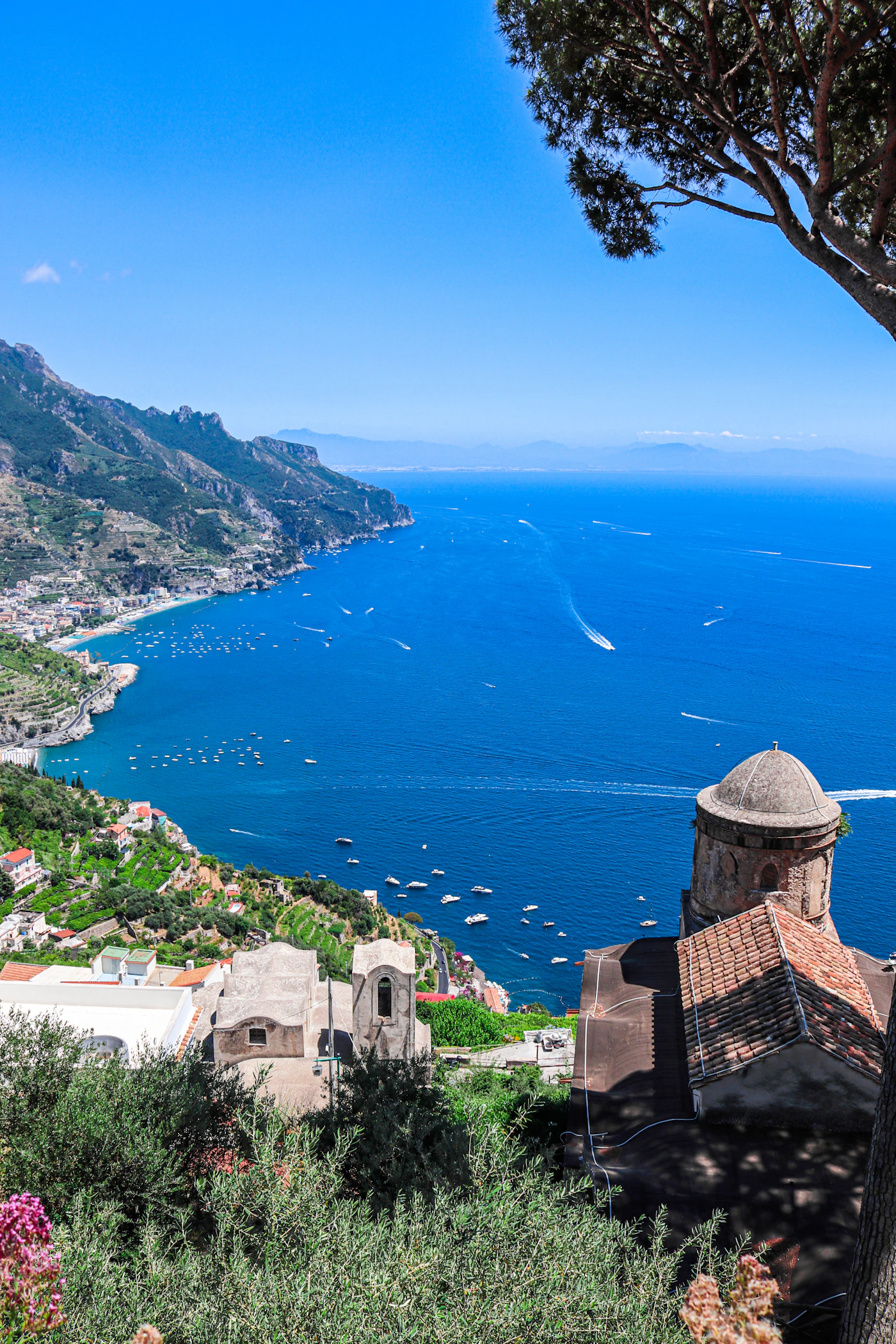View from Villa Rufolo Ravello looking out over the entire Amalfi Coast with ancient stone structures in the foreground and the deep blue Tyrrhenian Sea and boats stretching to the horizon below