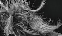 An intricate tangle of hair is captured in motion, with strands flowing dynamically in various directions. The detail in the texture of the hair is highlighted against a dark background, creating a sense of movement and energy.