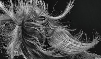 An intricate tangle of hair is captured in motion, with strands flowing dynamically in various directions. The detail in the texture of the hair is highlighted against a dark background, creating a sense of movement and energy.