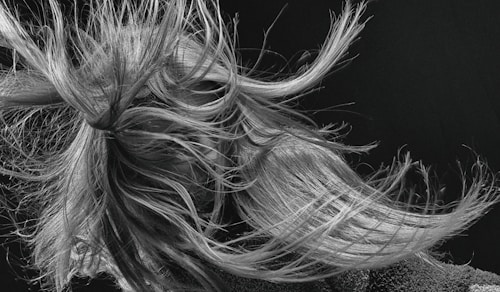 An intricate tangle of hair is captured in motion, with strands flowing dynamically in various directions. The detail in the texture of the hair is highlighted against a dark background, creating a sense of movement and energy.